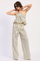 Woman wearing a Strapless cream and black striped peplum top with matching pants on a white background front view