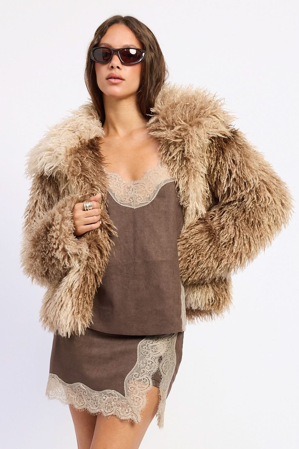 Woman wearing brown tie-dye oversized shaggy faux fur coat against white background.