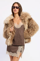 Woman wearing brown tie-dye oversized shaggy faux fur coat against white background.