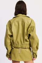 Woman wearing a faux leather green jacket and skirt with a white top on a light gray background