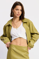 Woman wearing a faux leather green jacket and skirt with a white top on a light gray background