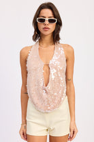 Woman wearing a sequin halter top and white shorts on a plain background