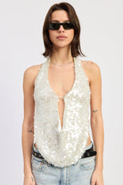 Woman wearing a white sequin halter top and jeans on a plain background front view