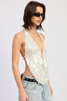 Woman wearing a white sequin halter top and jeans on a plain background side view