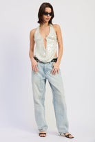 Woman wearing a white sequin halter top and jeans on a plain background front view