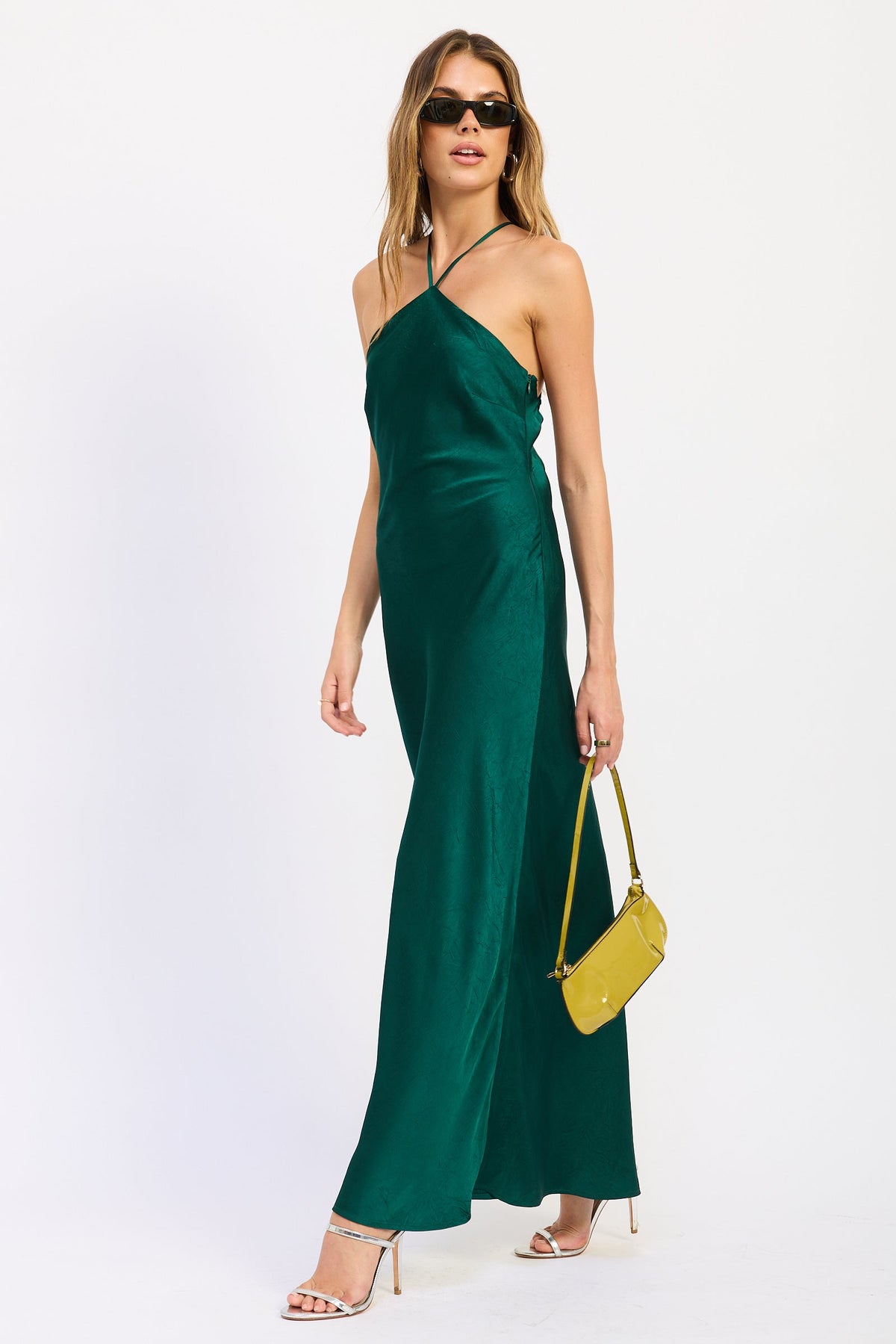 Angled front view of emerald green satin halter maxi dress showing sleek silhouette and subtle fabric texture