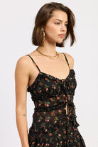 Woman wearing a black floral ruffle tie-front cami top on a white background 