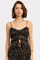 Woman wearing a black floral ruffle tie-front cami top on a white background 
