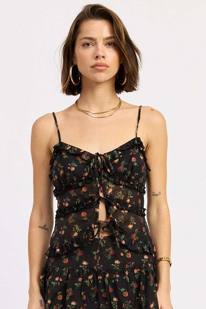 Woman wearing a black floral ruffle tie-front cami top on a white background 
