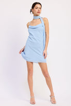 Woman wearing a light blue mini dress with cowl neckline and scarf on a white background front view