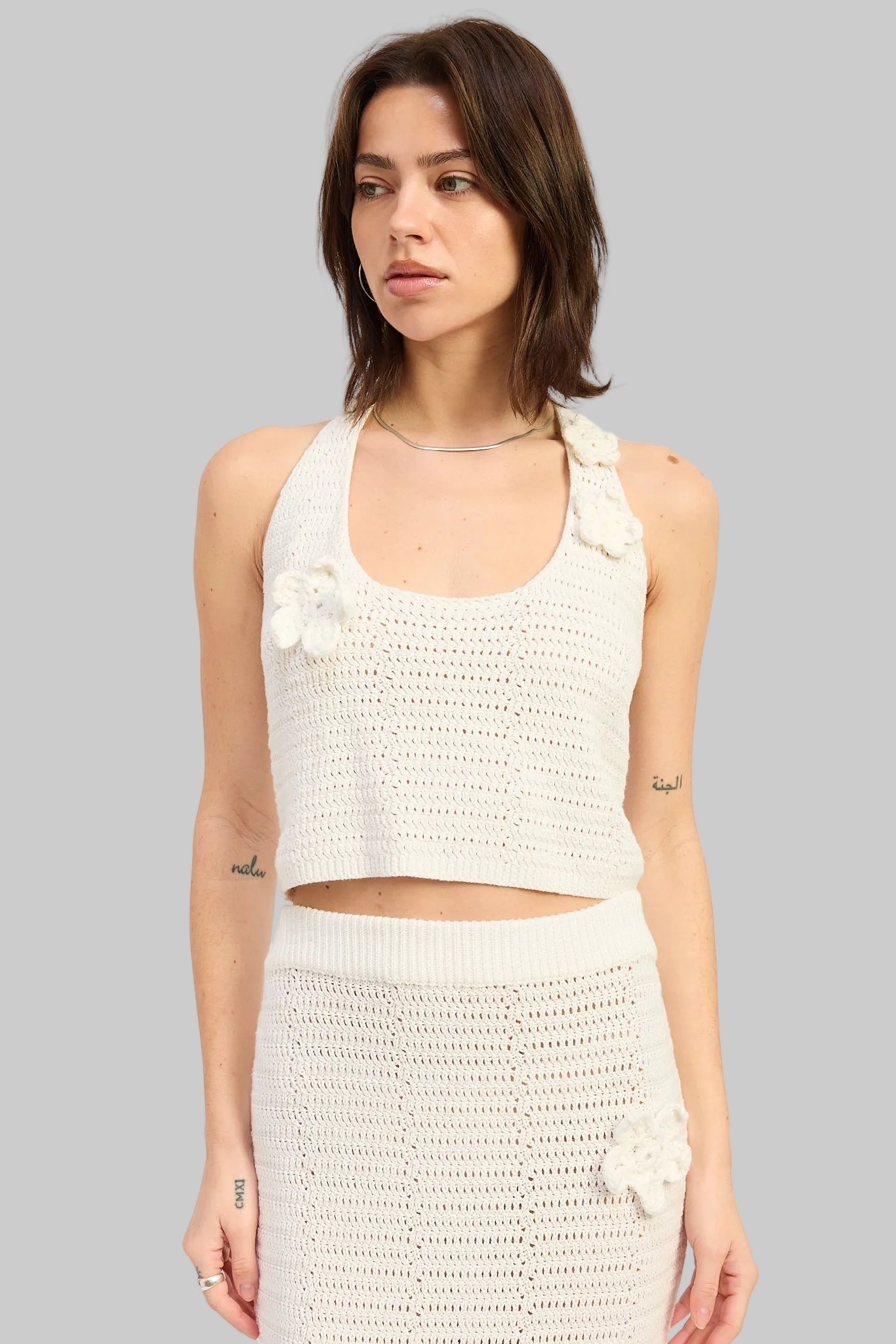 Woman wearing an ivory crochet halter crop top with floral applique details front view on a light gray background
