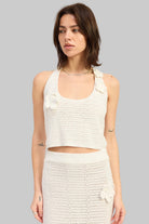 Woman wearing an ivory crochet halter crop top with floral applique details front view on a light gray background