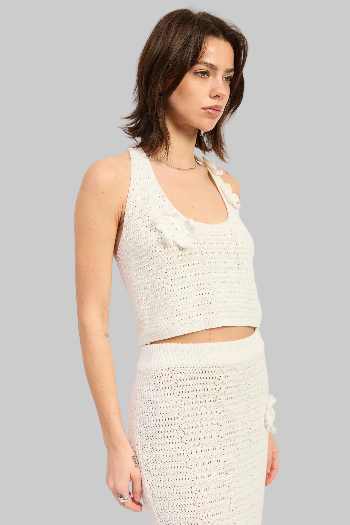 Woman wearing an ivory crochet halter crop top with floral applique details front view on a light gray background