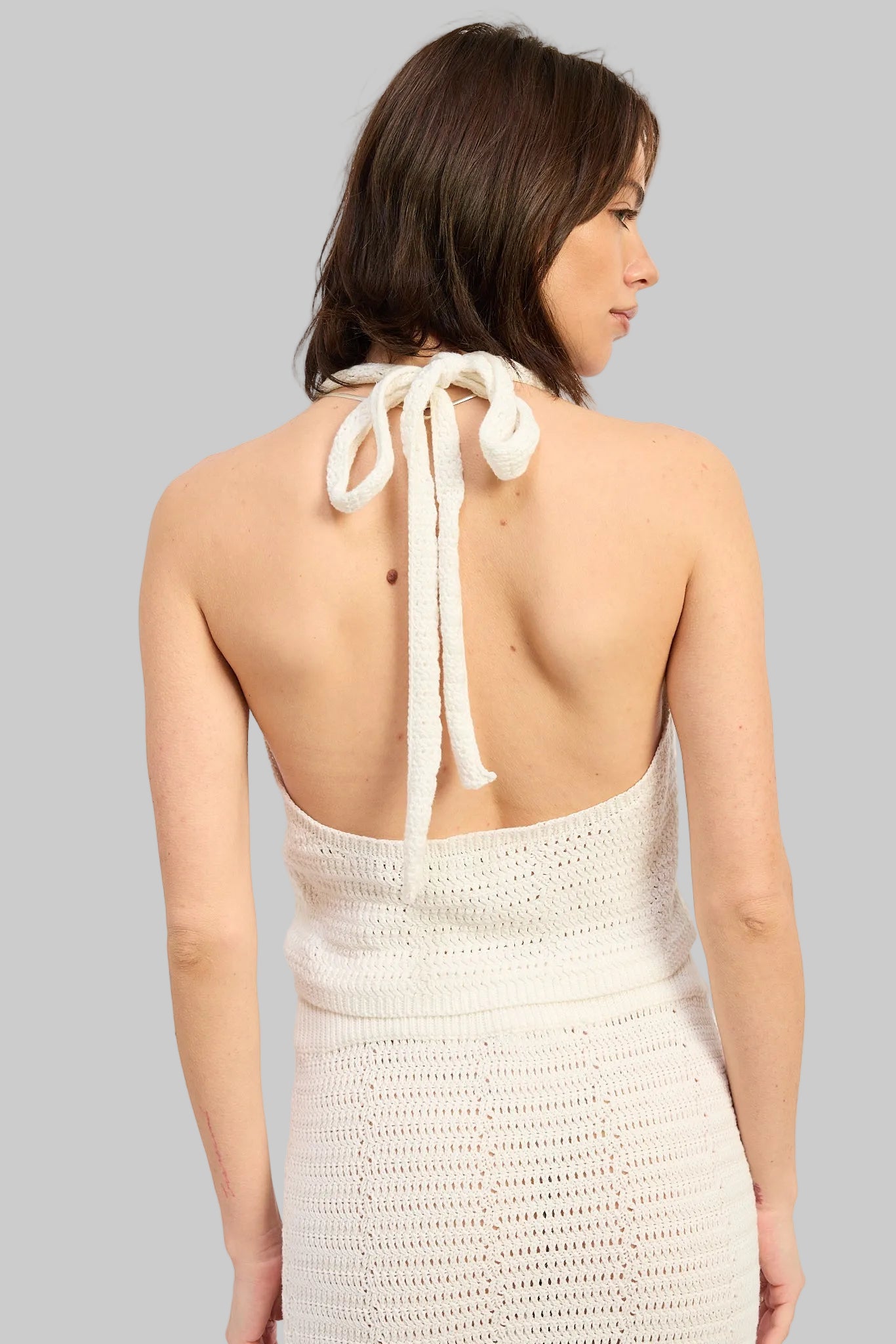 Woman wearing an ivory crochet halter crop top with floral applique details front view on a light gray background