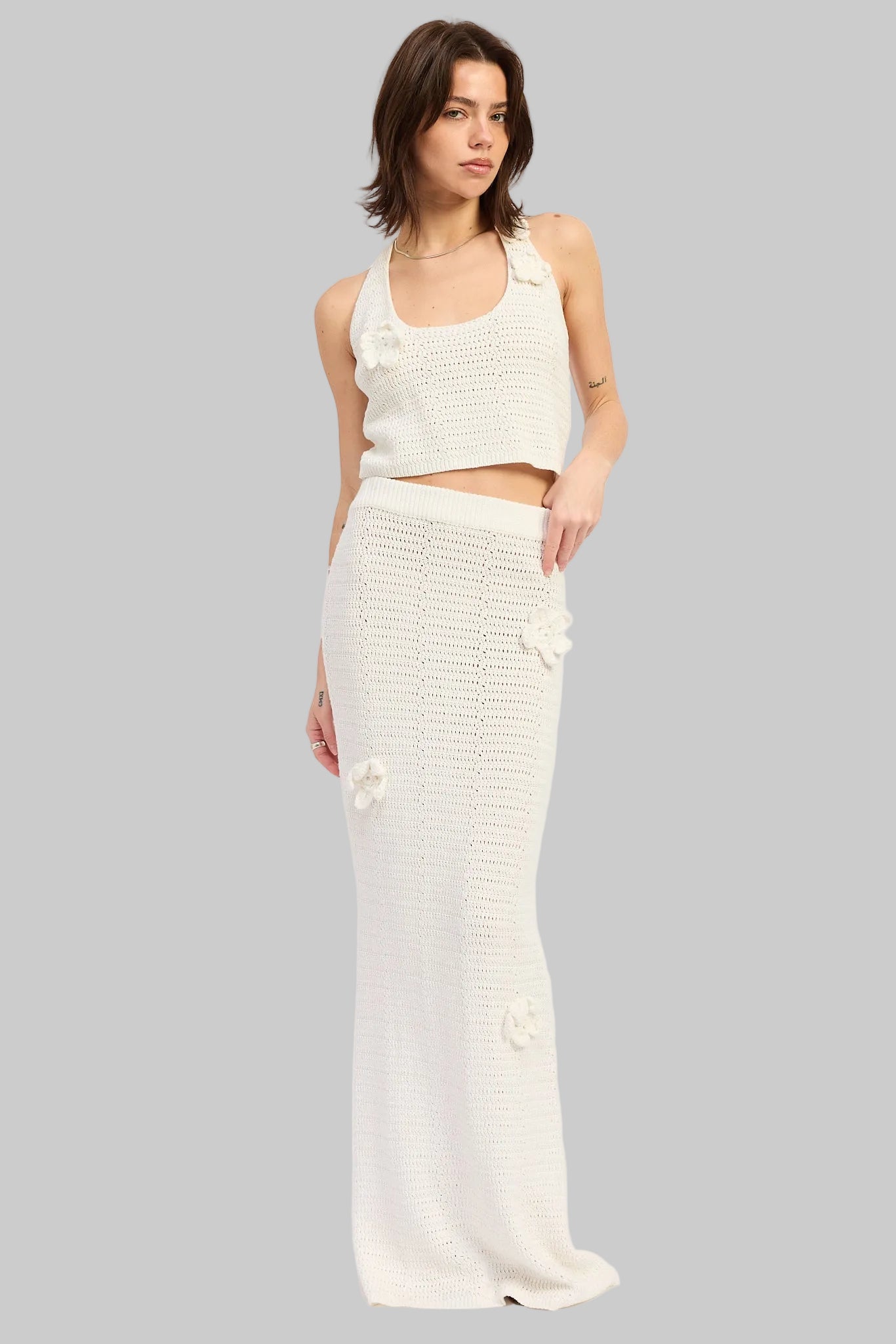 Woman wearing an ivory crochet halter crop top with floral applique details front view on a light gray background