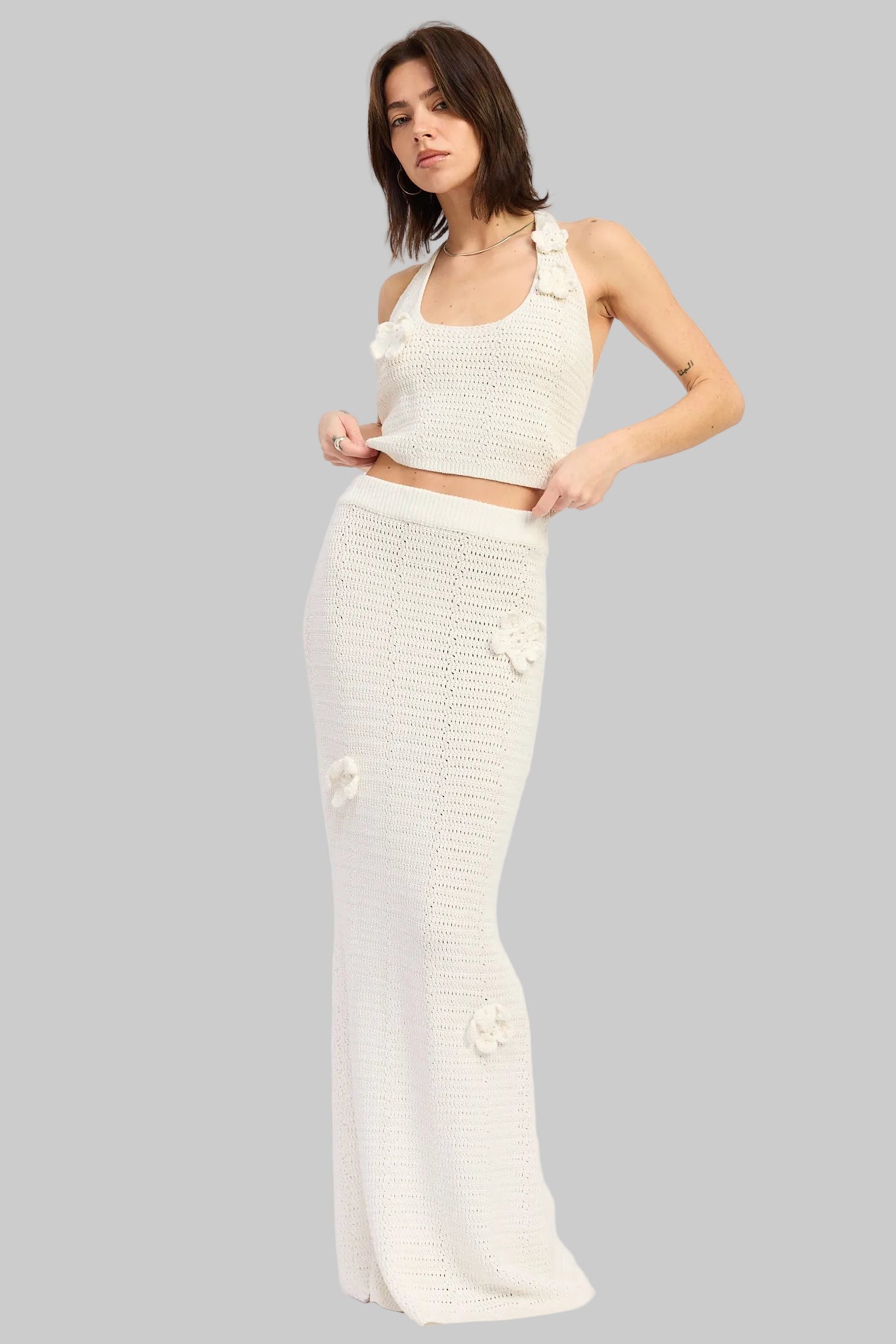 Woman wearing an ivory crochet top and ivory crochet maxi skirt with floral applique details set on a white background