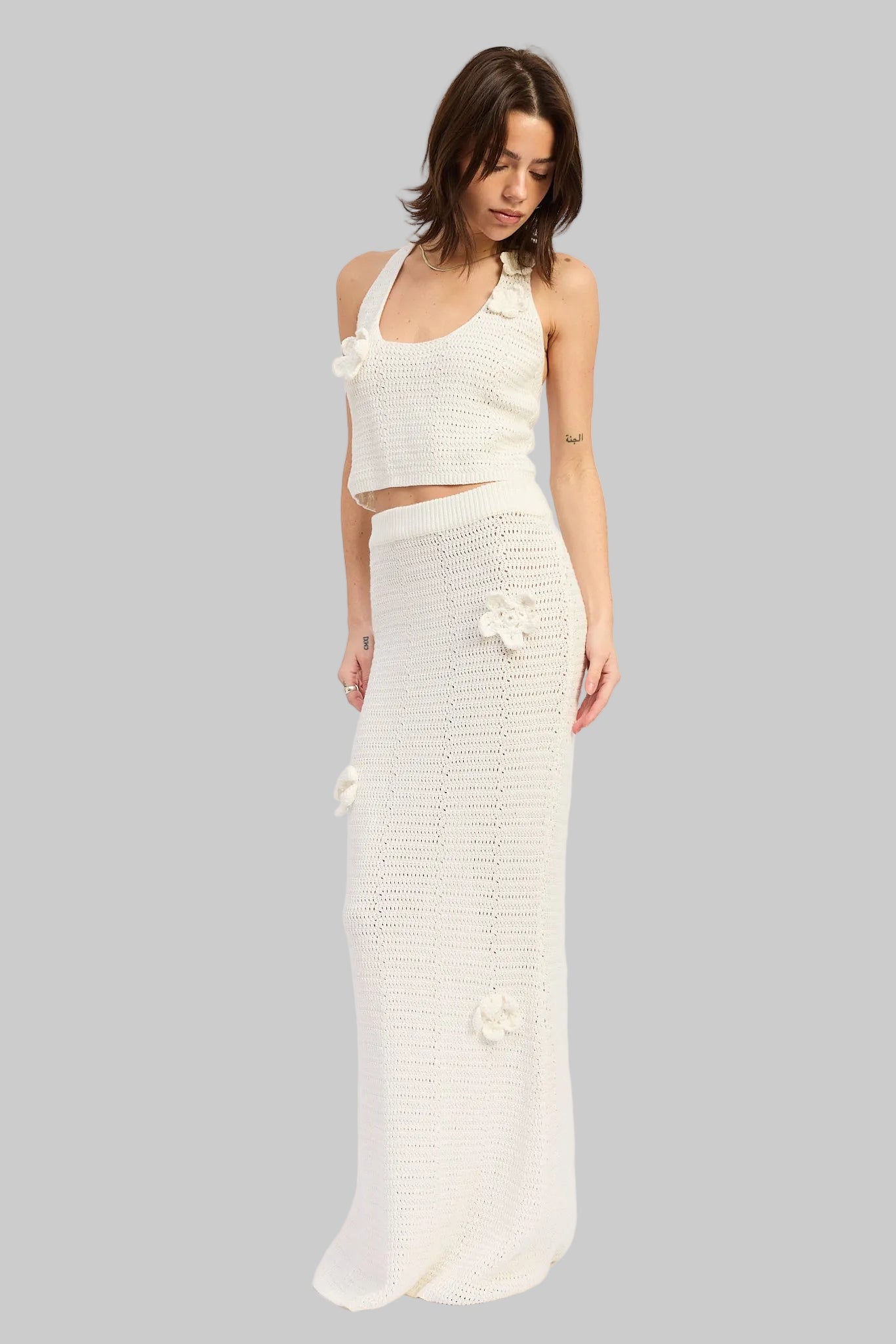 Woman wearing an ivory crochet top and ivory crochet maxi skirt with floral applique details set on a white background