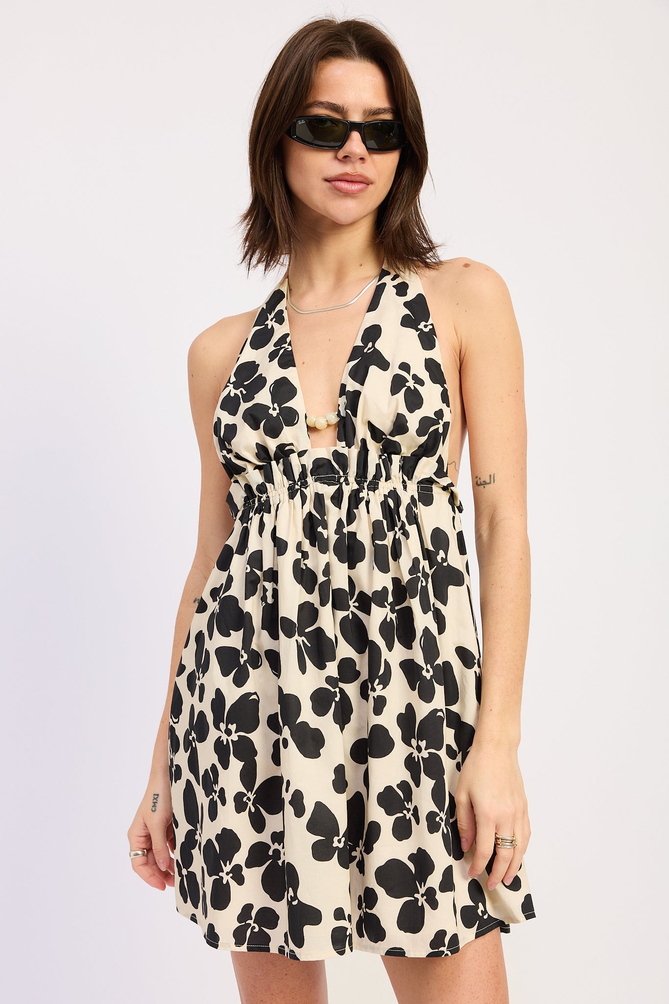 Woman wearing a black floral halter mini dress front view flowy silhouette on a plain background