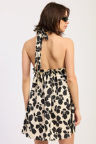 Woman wearing a black floral halter mini dress back view flowy silhouette on a plain background