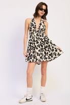 Woman wearing a black floral halter mini dress front view flowy silhouette with white sneakers on a plain background