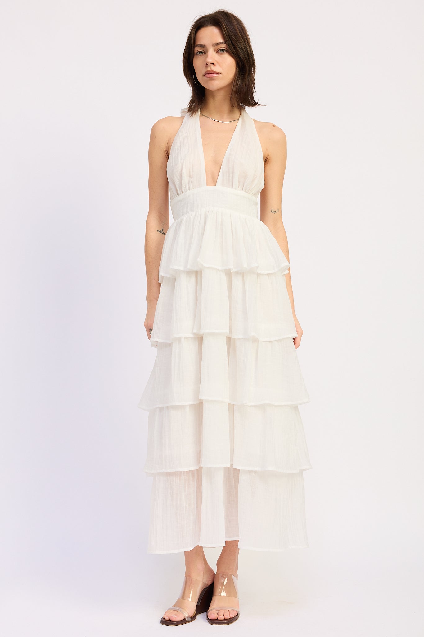 Model wearing the Ivory Cascade Tiered Maxi Dress featuring a halter neckline, plunging V neckline, open back, and layered tiered skirt in a soft ivory textured fabric.