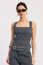 Woman wearing a washed charcoal denim corset top with buckle detail front view with sunglasses on a plain background