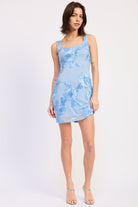 Woman wearing a light blue floral embroidered mesh mini dress with appliqué detail and open back on a white background front view