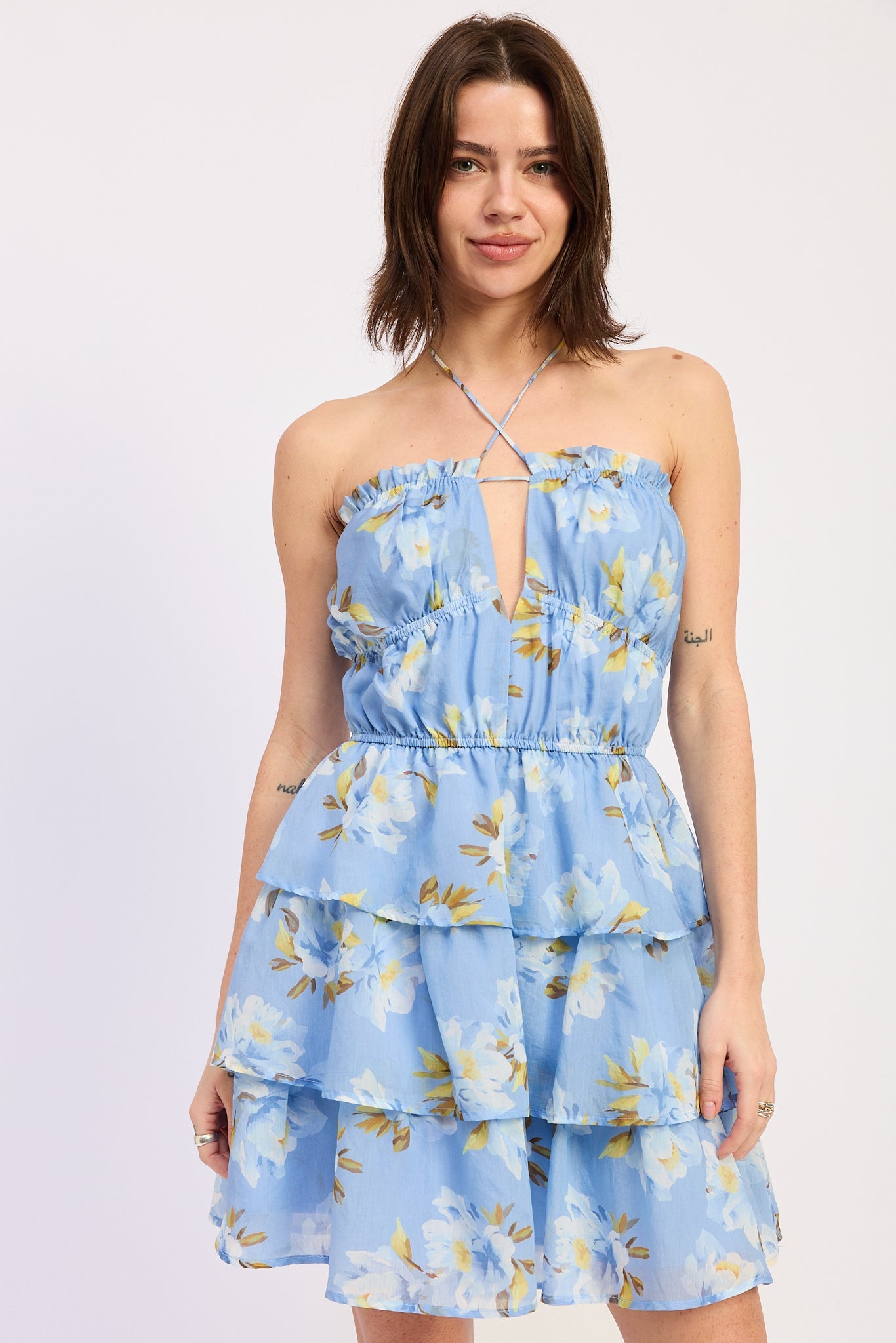 Woman wearing a blue floral ruffle tiered mini dress against a white background front view