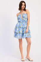 Woman wearing a blue floral ruffle tiered mini dress against a white background front view
