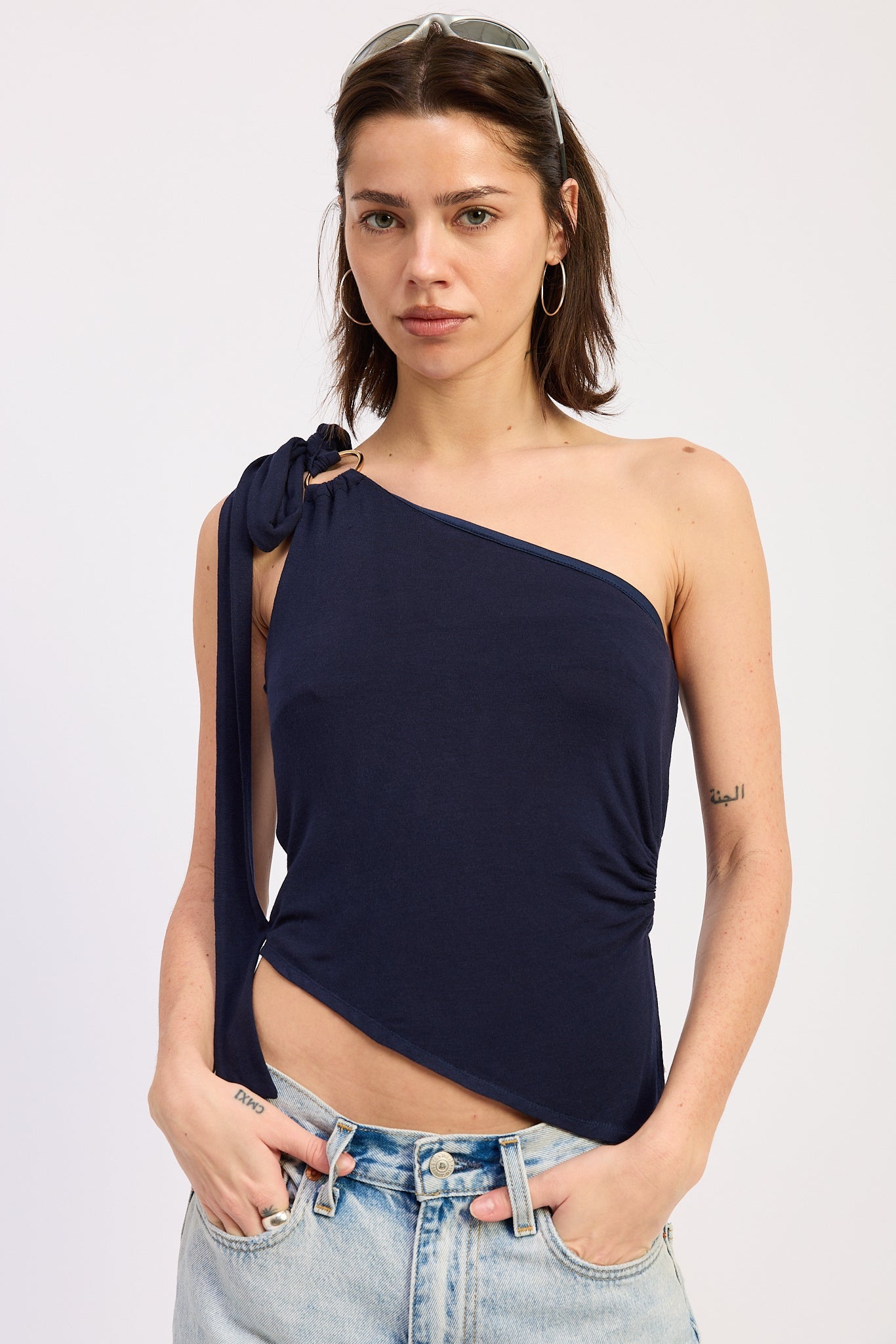 Woman wearing a navy one-shoulder top with denim shorts on a light gray background