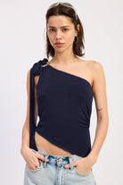 Woman wearing a navy one-shoulder top with denim shorts on a light gray background