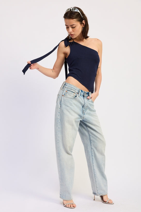 Woman wearing a navy one-shoulder top and light blue jeans on a white background