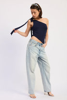 Woman wearing a navy one-shoulder top and light blue jeans on a white background