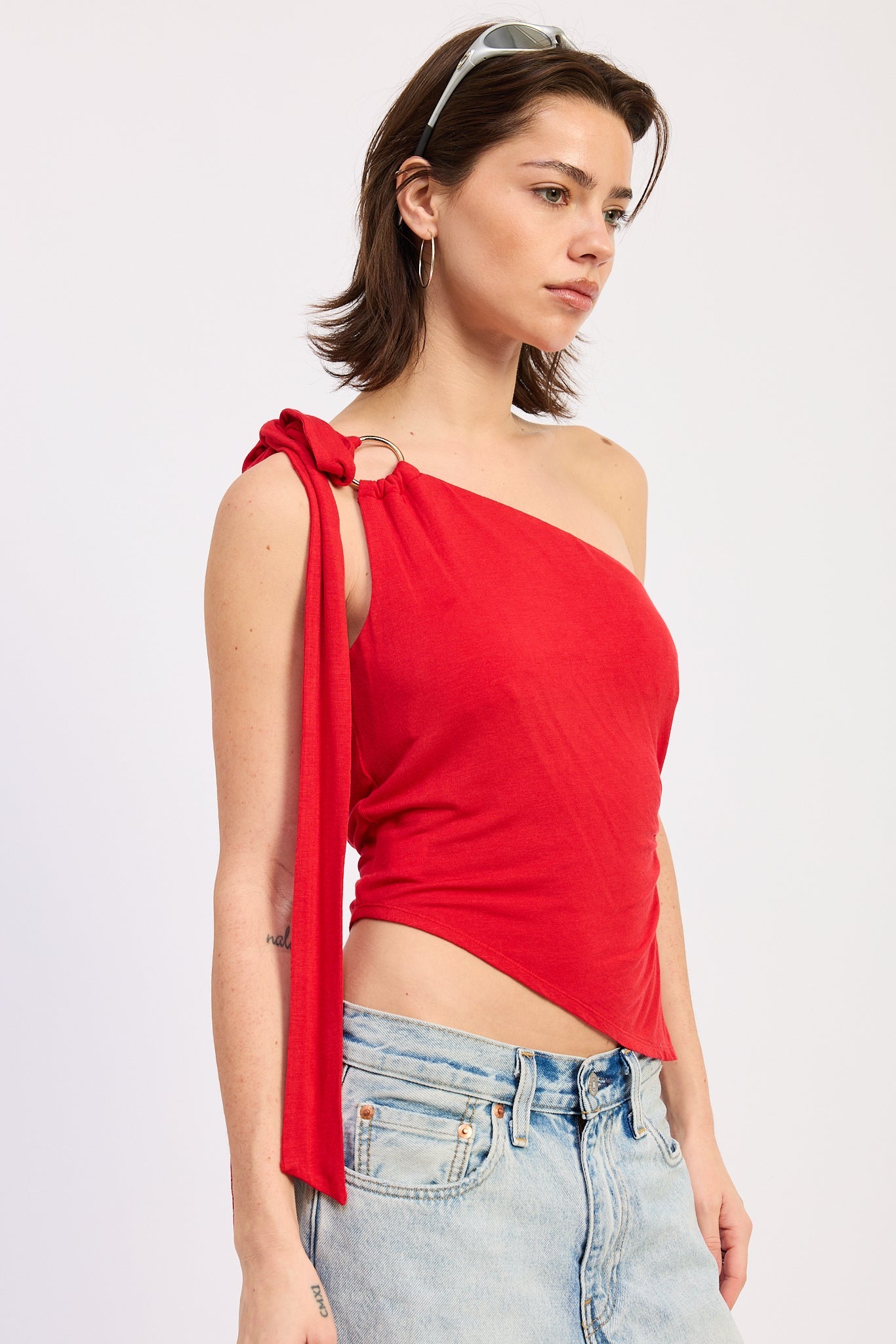 Woman wearing a red one-shoulder top with tied detail on a plain background
