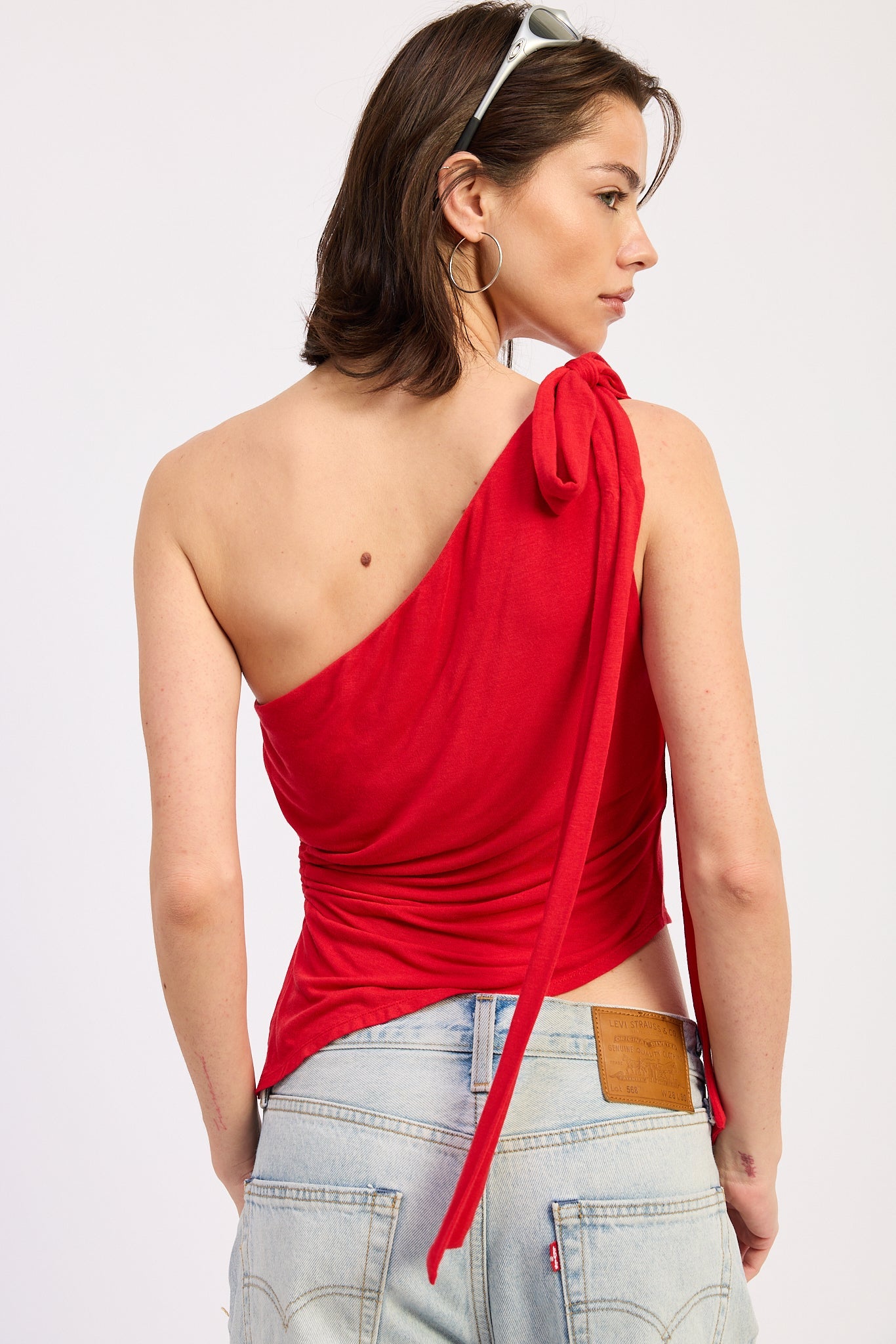 Woman wearing a red one-shoulder top and light blue jeans on a white background