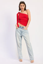 Woman wearing a red top one shoulder top and light jeans on a white background