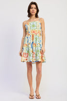 Woman wearing a scarf-inspired print blend of palm motifs and delicate detailing for a vibrant colorful floral tiered mini dress on a white background front view