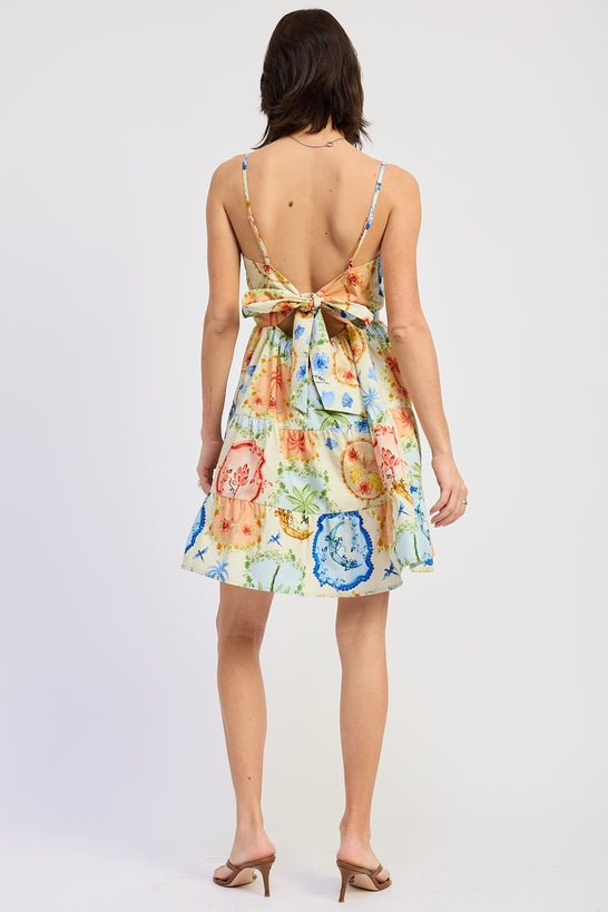 Woman wearing a scarf-inspired print blend of palm motifs and delicate detailing for a vibrant colorful floral tiered mini dress with spaghetti straps on a white background back view