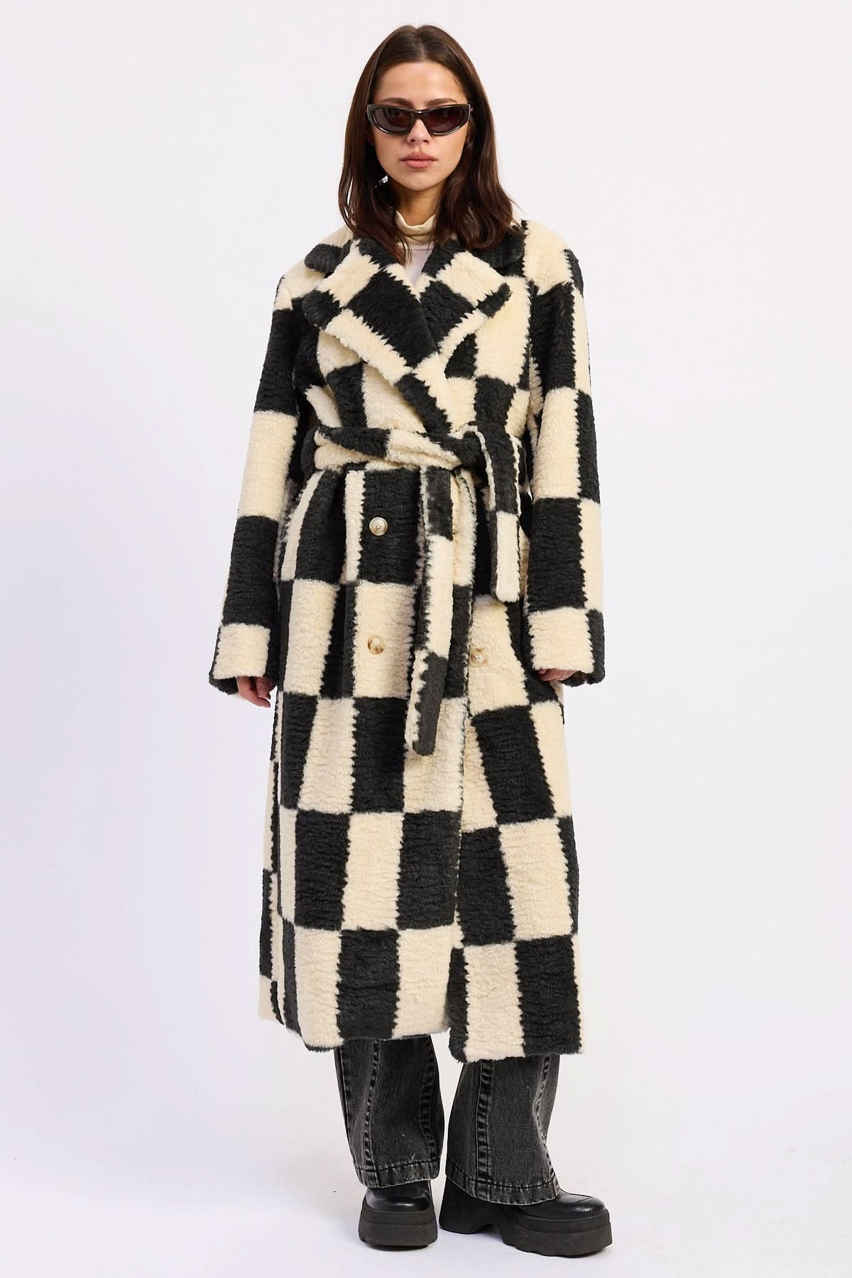 Woman wearing ivory and black checkered faux fur coat with wide collar and waist tie against white background.