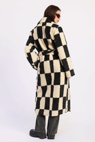 Woman wearing ivory and black checkered faux fur coat, back view with matching belt against white background.