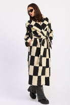 Woman wearing ivory and black checkered coat with wide lapels and side pockets against white background.