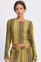 Woman wearing green and brown striped cropped crochet top with long sleeves against white background.