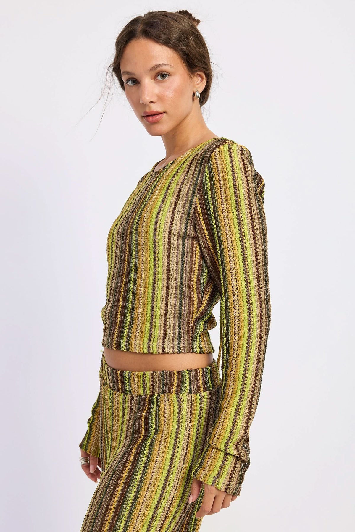 Woman wearing green and brown crochet top, side view showing cropped hem against white background.
