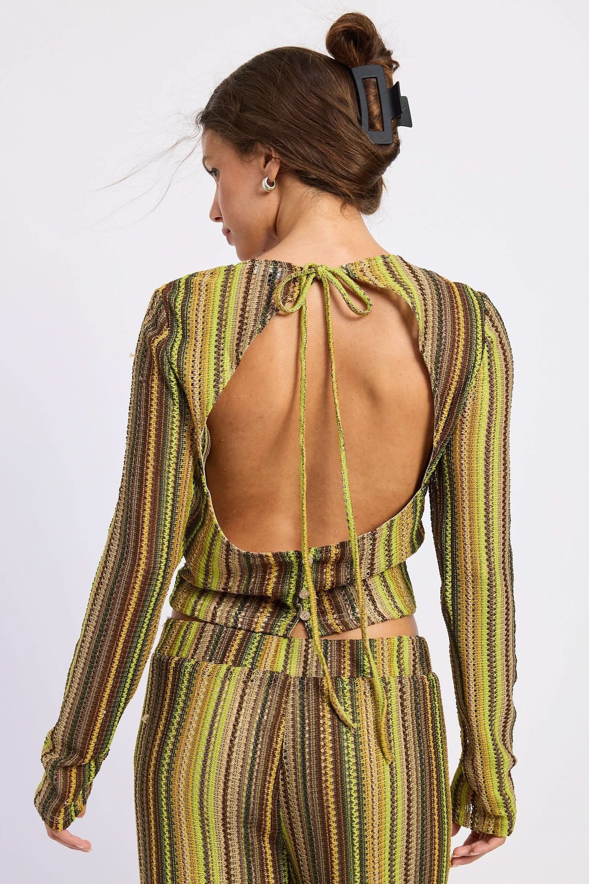 Woman wearing green and brown crochet top, back view showing open back and neck tie against white background.