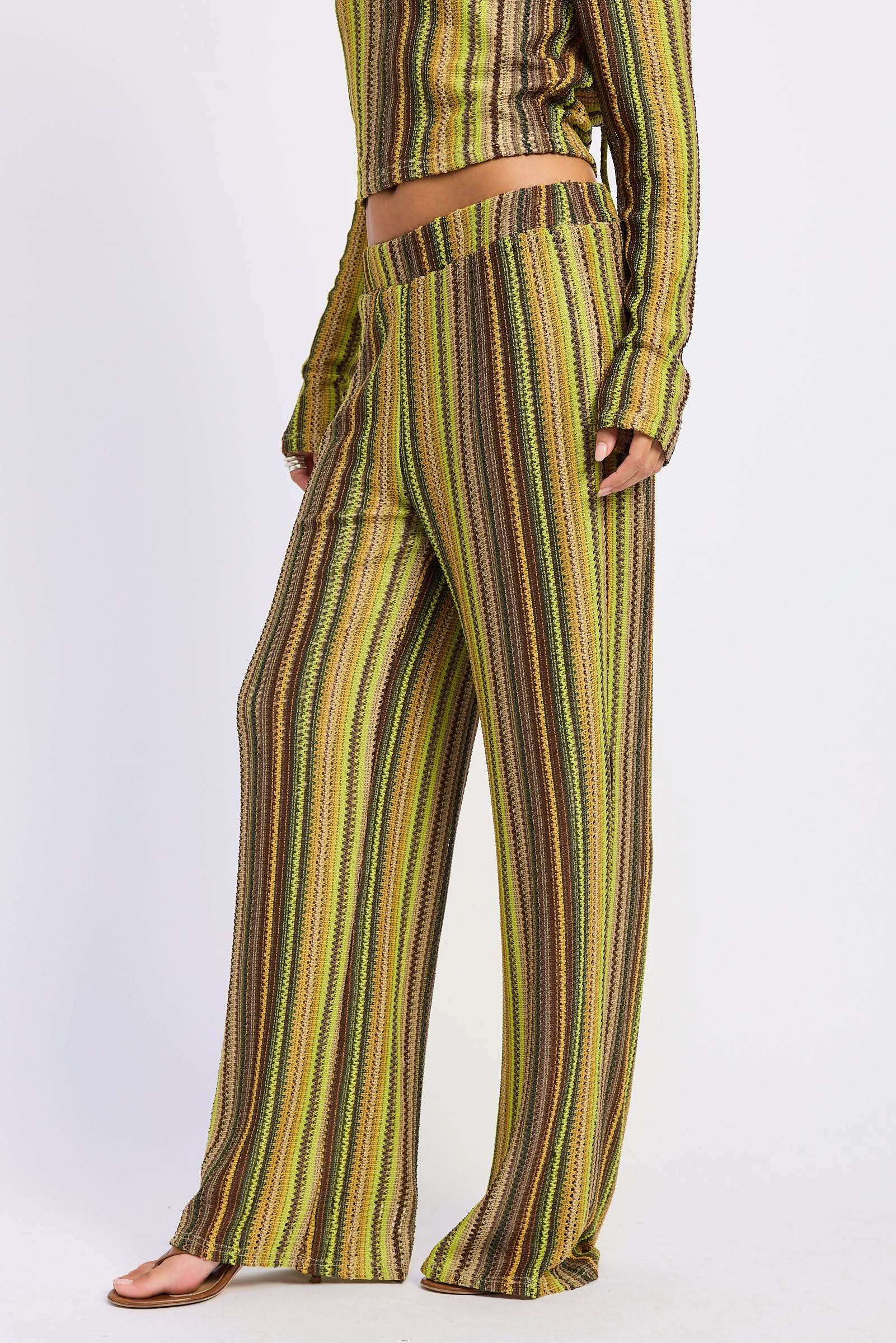 Woman wearing green and brown crochet pants, close view showing low-rise waist and wide legs against white background.