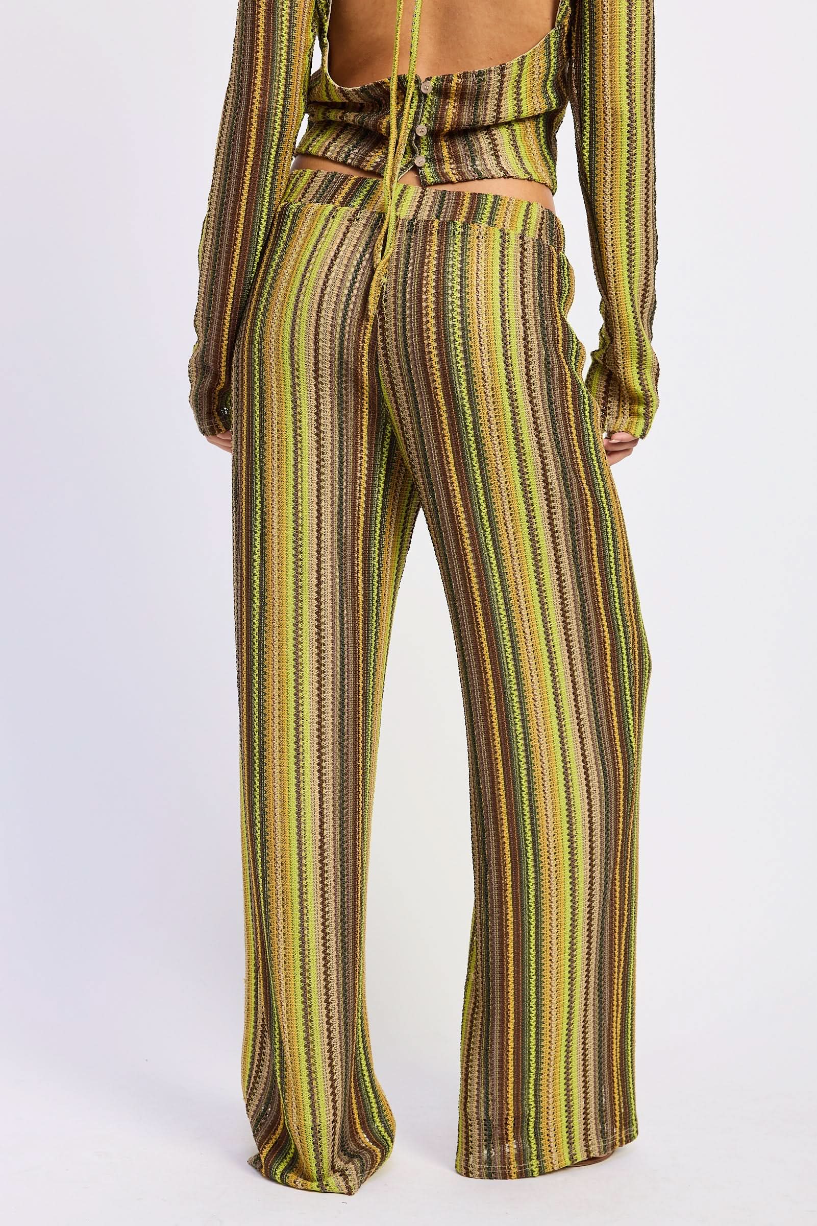 Woman wearing green and brown striped crochet wide-leg pants, back view against white background.