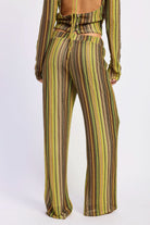 Woman wearing green and brown striped crochet wide-leg pants, back view against white background.