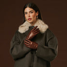 Woman wearing a dark coat with a fur collar and brown leather gloves on a brown background