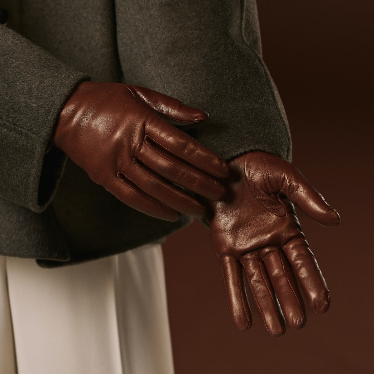 Brown leather gloves worn by a person against a dark background