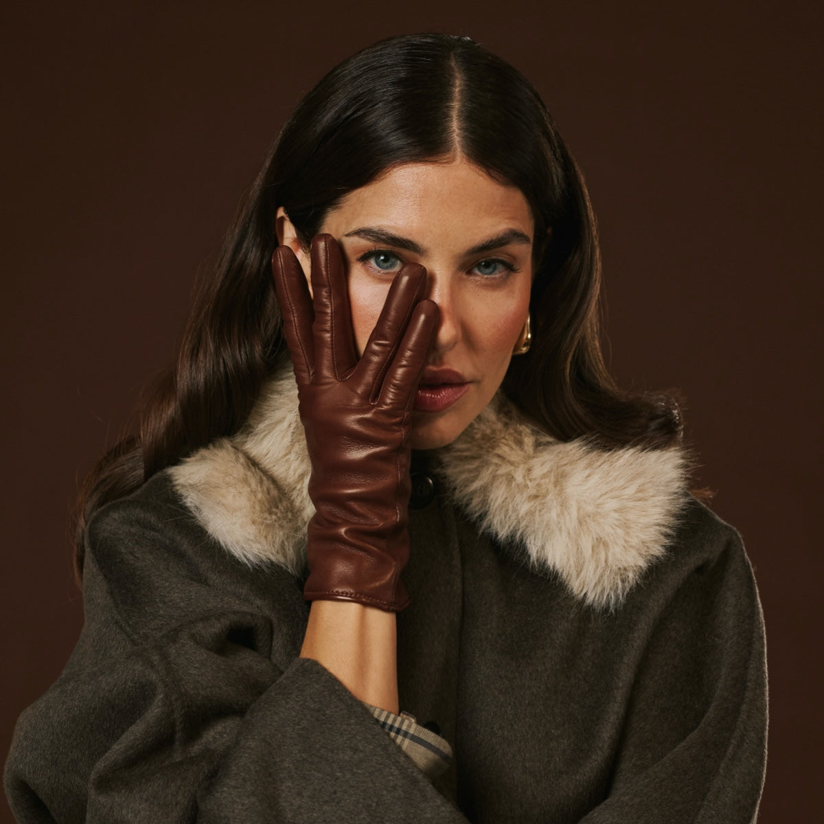 Woman wearing a brown leather glove and a fur-lined coat against a dark background